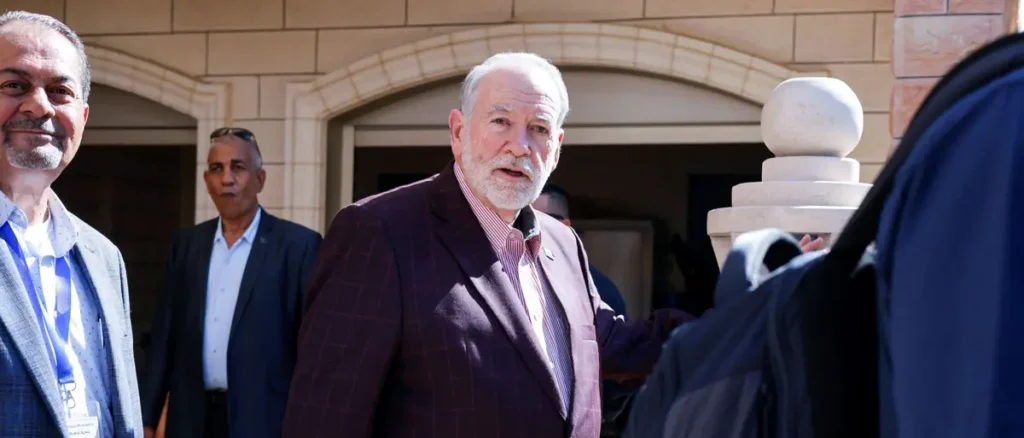 A man in a suit is seen walking outside a building, surrounded by other individuals.