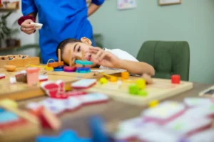 A child is engaged in a hands-on activity with colorful wooden blocks and toys at a table, with an adult standing nearby.
