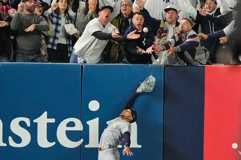 A baseball player leaps to catch a ball as fans in the stands react with excitement.