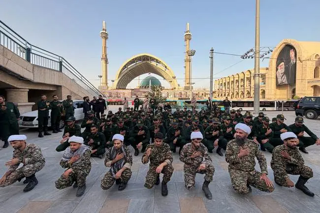 A group of uniformed personnel kneel and place their hands on their chests in a solemn gesture in front of a mosque.