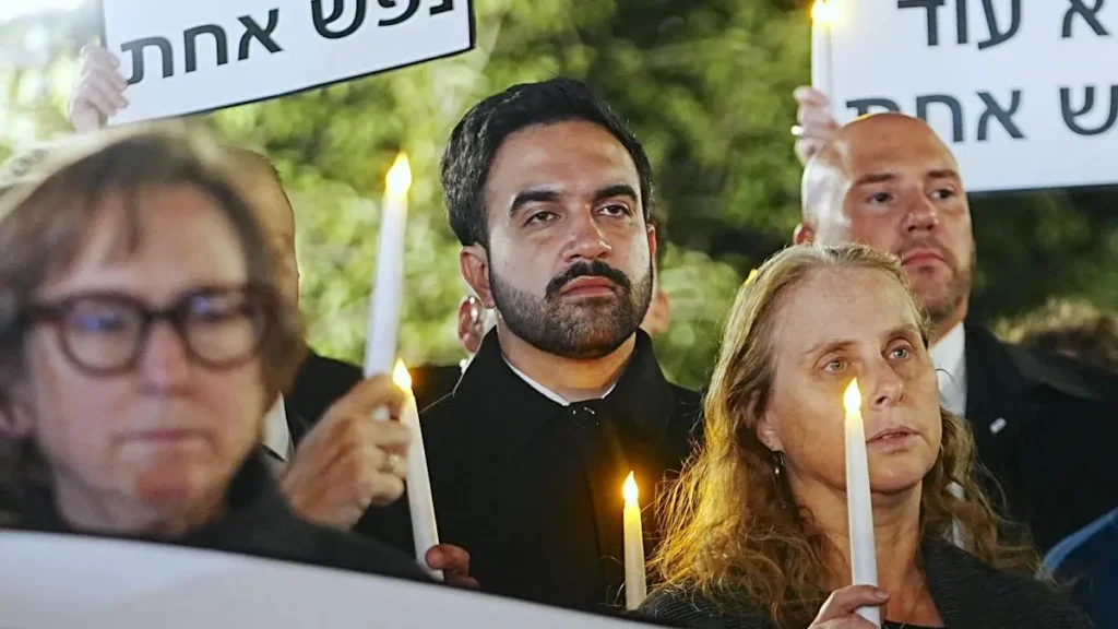 A group of people hold candles and signs during a vigil or memorial event.