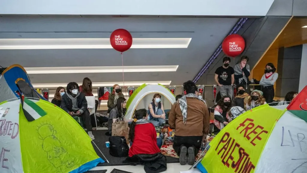 A group of people are gathered in a tented protest at The New School, advocating for Palestinian freedom and other causes.