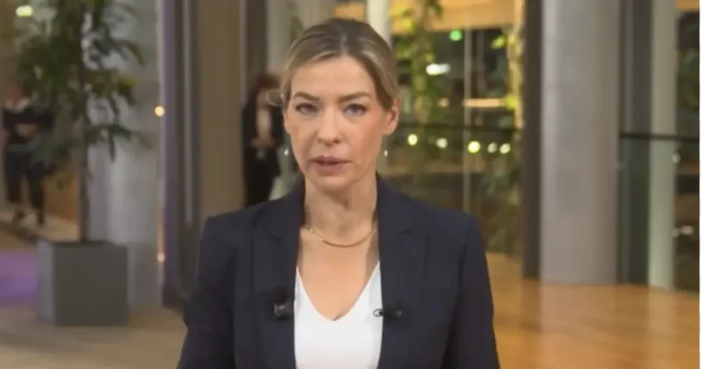 A news anchor is delivering a report in a professional setting with a modern background.