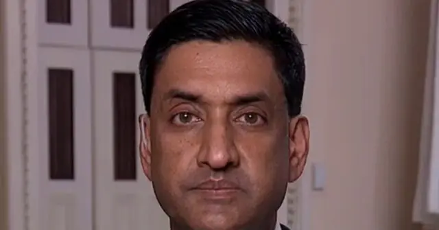 The image shows a close-up of a man with a serious expression, set against a background that includes a door with a grid pattern.