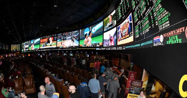 The image shows a bustling sportsbook with numerous screens displaying live sports action and a crowd of people engaging in various activities.