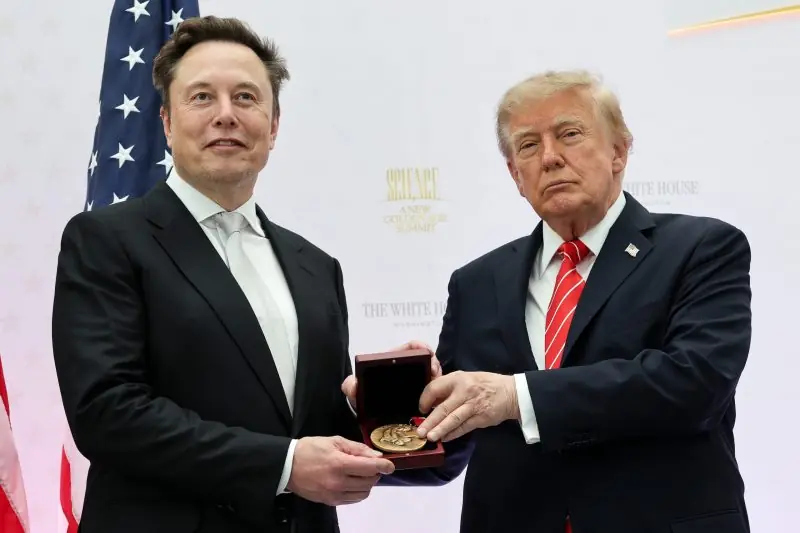 The image shows two individuals in formal attire, one presenting a medal to the other, with an American flag and a backdrop indicating a formal event at the White House.