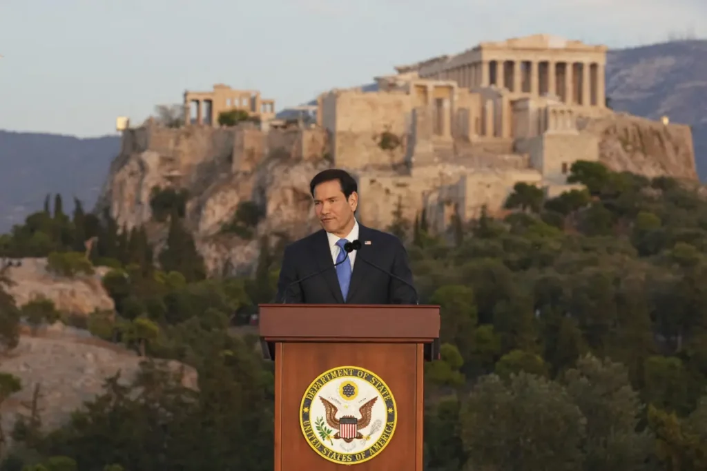 A man stands at a podium with the U.S. Department of State seal, delivering a speech in front of the Acropolis in Athens, Greece.