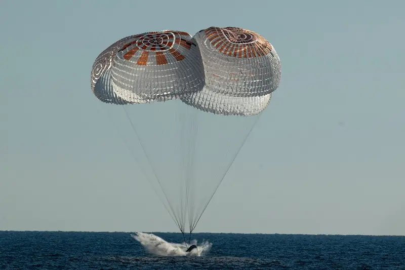 A spacecraft is seen landing in the ocean with its parachutes fully deployed.