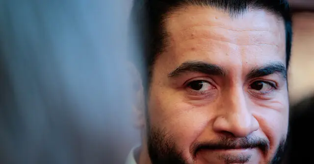 The image shows a close-up of a person with a serious expression, set against a blurred background.