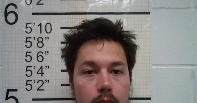 The image appears to be a mugshot of a person standing in front of a height chart.