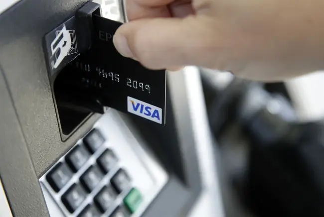A person is inserting a Visa credit card into an ATM machine.