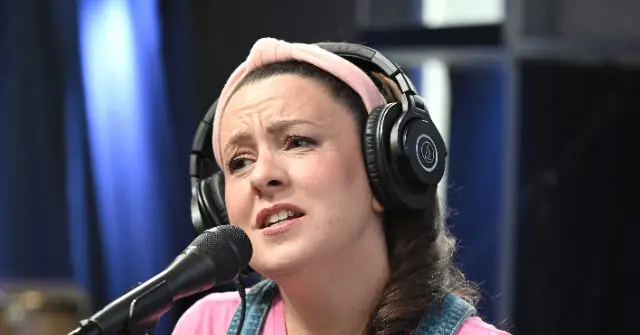 A person wearing headphones and a pink headband is speaking into a microphone in what appears to be a radio or recording studio setting.