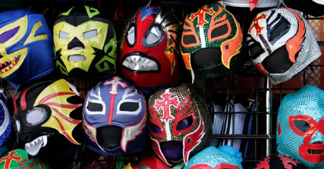 The image shows a collection of colorful wrestling masks, each with unique designs and patterns, displayed on a rack.