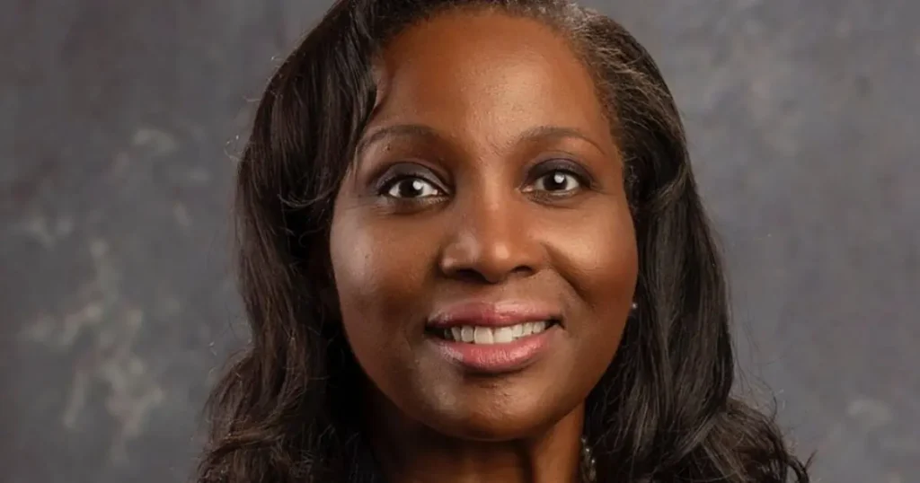 The image shows a close-up portrait of a smiling individual with long, dark hair against a neutral background.