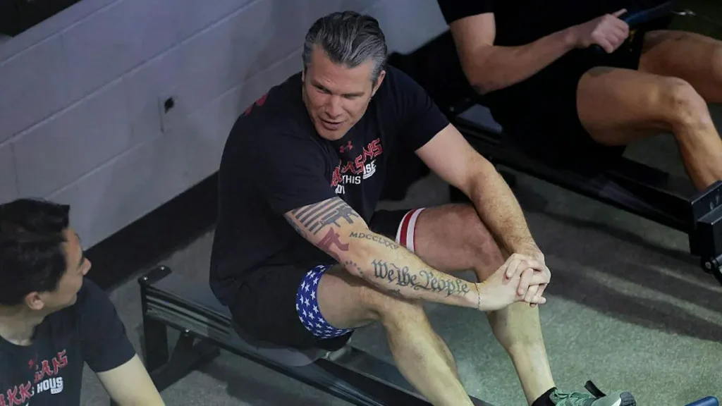 A man is seen in a gym setting, possibly during a workout or training session, with another individual observing.