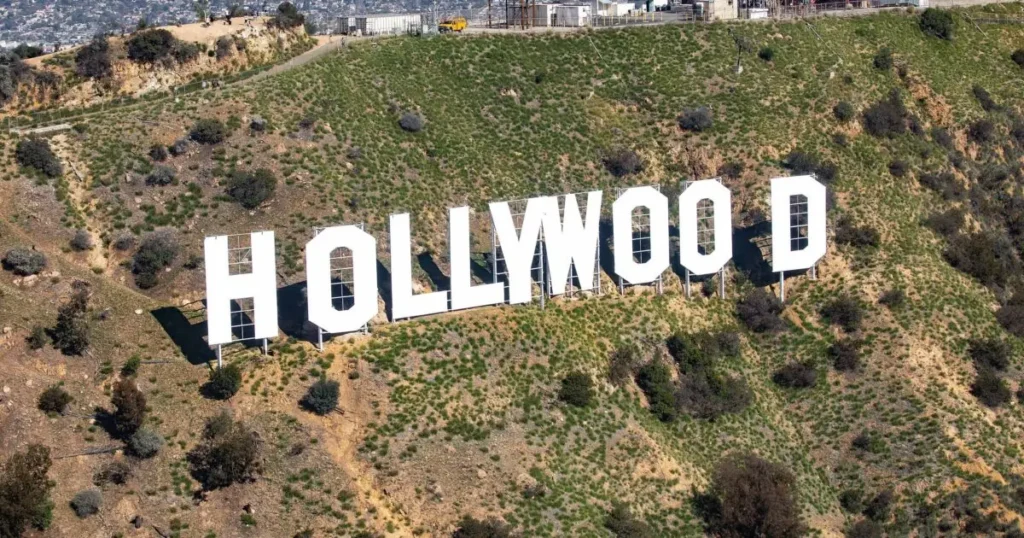 The iconic Hollywood sign is prominently displayed on a hillside, surrounded by sparse vegetation.