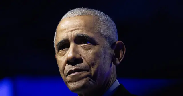 The image shows a close-up of a man in a suit, with a serious expression, set against a dark background with blue lighting.