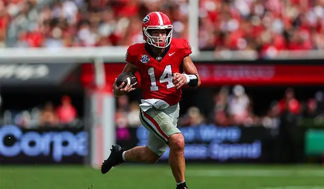 A football player in a red uniform with the number 14 runs with the ball during a game.