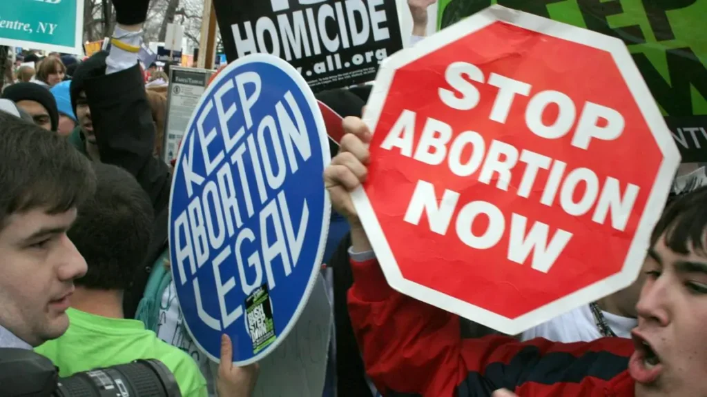 The photo depicts a protest with signs advocating for the legalization of abortion and opposing it.