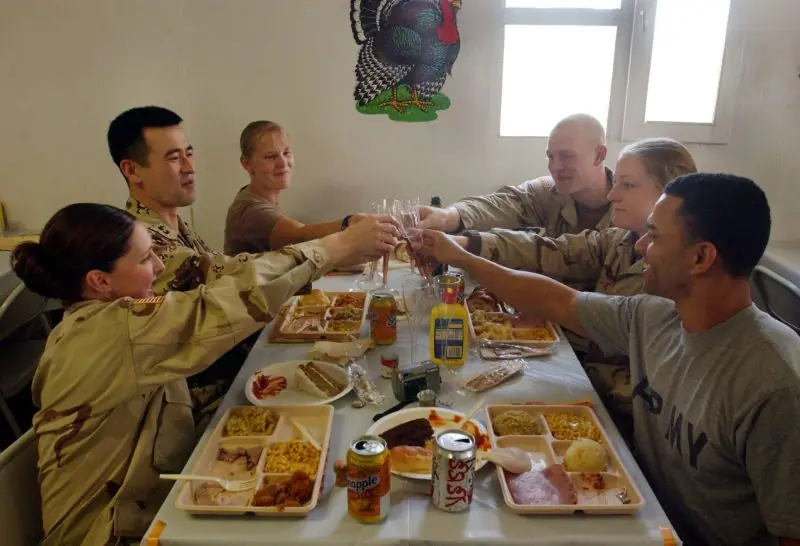A group of military personnel toasts during a meal, celebrating together in a communal dining setting.