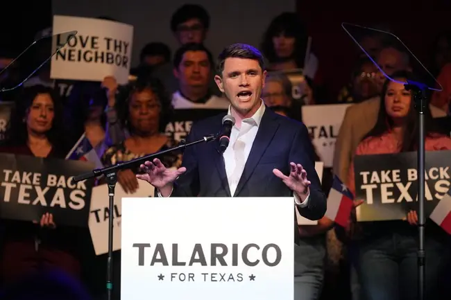 A candidate named Talarico is giving a speech at a campaign rally in Texas, with supporters holding signs in the background.