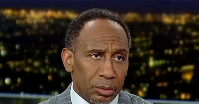 The image shows a man in a suit and tie, appearing to be on a news broadcast with a cityscape in the background.