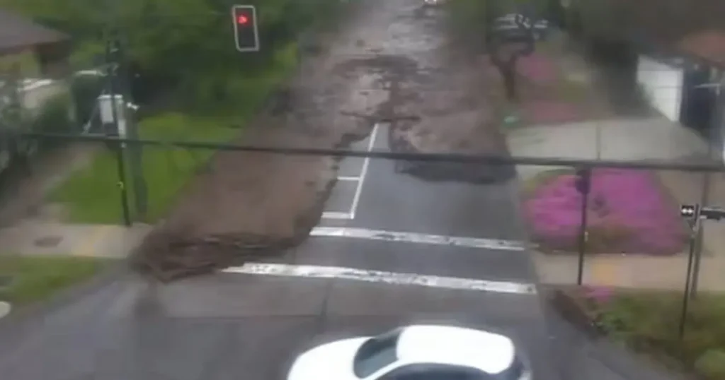A flooded street with a red traffic light and a partially submerged car is visible, indicating severe flooding in the area.